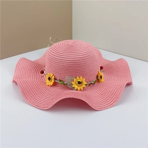 Detailed view of pink straw hat with wavy brim and realistic sunflower wreath decoration