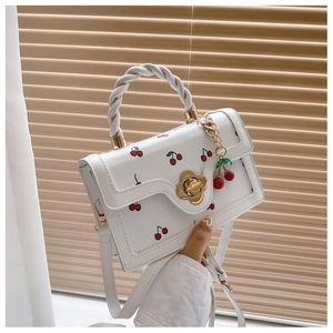 Detail of white leather handbag with red cherry patterns and gold petal shaped turn lock