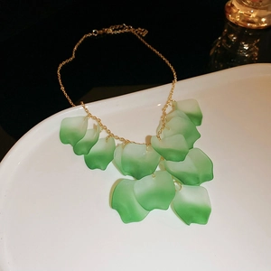 Detail of green petal tassel necklace with gold chain on a white ceramic plate