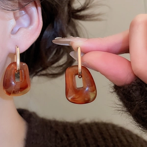 Close-up of amber acrylic square drop earrings with gold metal bar details