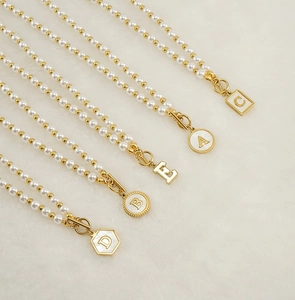 Détail d'un collier de perles avec pendentifs lettres dorées et fermoir à bascule sur tissu