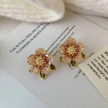 Detailed shot of champagne floral earrings with gold accents on a poetic art card background