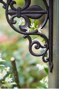 Close-up of vintage cast iron fleur-de-lis wall bracket mounted on rustic wood pillar