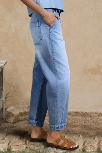 Détail d'un jean large bleu clair avec poches cargo sur un fond texturé et naturel