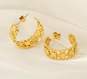 Detail of gold-plated hollow floral pattern C-shaped earrings on white silk