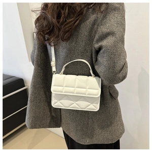 Detail of white quilted handbag with gold hardware and top handle on a blazer
