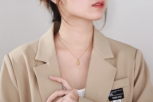 Gros plan d'un collier pendentif ovale doré vintage sur un mannequin en veste beige