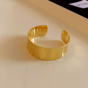 Detailed view of a wide gold cuff bracelet featuring vertical textured wave patterns