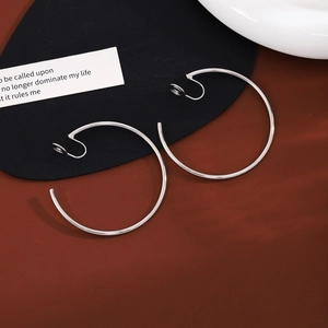 Close-up of large silver hoop clip-on earrings on a vintage textured surface