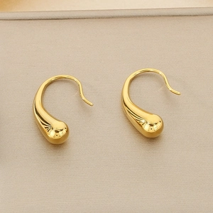 Detailed view of gold teardrop earrings with mirror-polished finish on beige texture