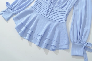 Détail du haut bleu clair avec taille plissée, ourlet basque et nœuds aux poignets
