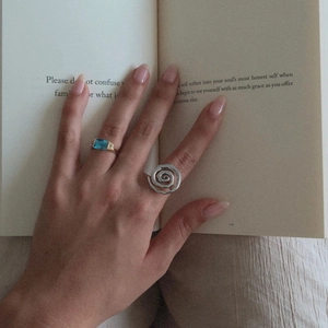 Detail of a silver spiral ring and a gold ring with rectangular blue gemstone on a hand