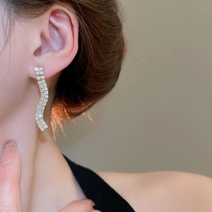 Close-up of elegant gold S-shaped wave earrings with sparkling pavé rhinestones
