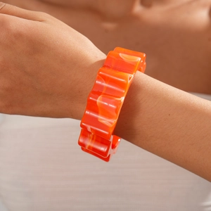 Close-up of a bold orange wavy acrylic cuff bracelet with marble texture and glossy finish