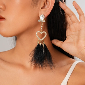 Close-up of heart tassel earring with crystal accents and black feather on model