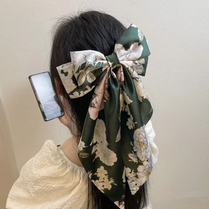 Detail of dark green satin bow hair clip with camellia pattern worn on long hair