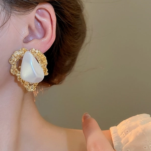 Gros plan de boucles d'oreilles baroques en or martelé avec une grande perle blanche