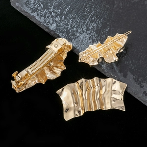 Golden irregular wavy metal hair clip set with pleated texture on dark stone background
