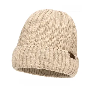 Detail of beige ribbed knit beanie featuring a brown leather accent tag on white background
