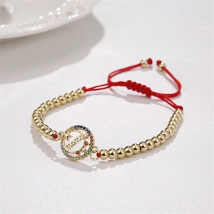 Detail of adjustable gold-plated MAMA bracelet with colorful zircons and red woven cord