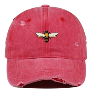Detail of bee embroidery and distressed holes on washed rose red cotton baseball cap
