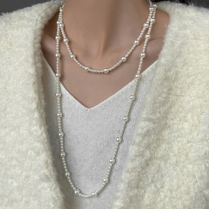 Close-up of elegant double-layered long pearl necklace on model with white knitwear
