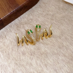 Détail de boucles d'oreilles serpent dorées avec yeux en cristal vert et strass