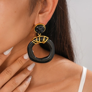 Close-up of oversized black resin hoop earrings with gold metal accents on a model