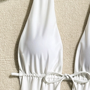 Detail of white halter neck swimsuit featuring drawstring bow and glossy satin fabric