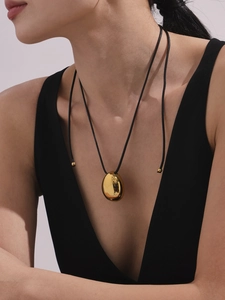 Macro detail of a 18k gold-plated teardrop pendant on a minimalist black cord necklace