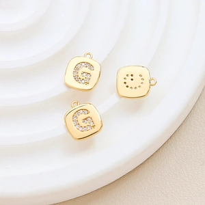 Macro shot of gold-plated square G pendant with sparkling zircon and smile face reverse