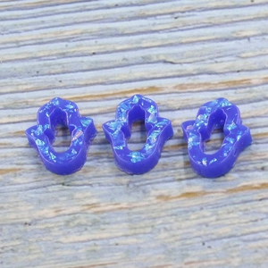 Close-up of three blue glitter resin Hamsa hand charms on a blue wood background