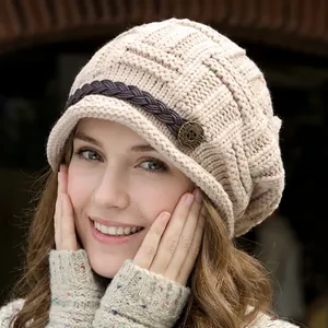 Close-up of beige knit beanie with woven leather strap and vintage metal button detail
