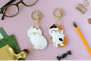 Vue à plat de porte-clés chat en cuir avec papeterie sur un fond rose tendre