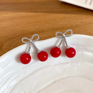Macro detail of red cherry earrings with silver bow design on a white textured plate