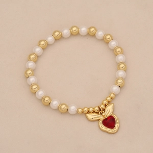 Detailed macro view of a pearl and gold bead bracelet featuring a red heart charm