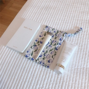 Flat lay of floral cotton pouch with makeup brush, cleanser and white notebook