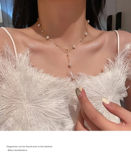 Detail of a golden Y-shaped necklace with elegant white pearls on a model wearing white feathers