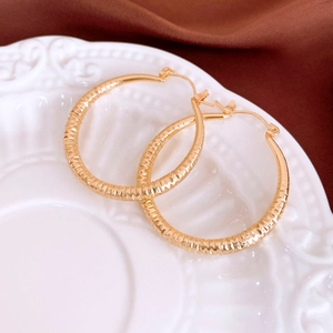 Macro shot of gold hoop earrings featuring a diamond hammered texture on a ceramic tray