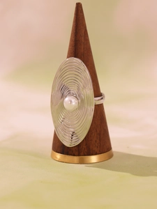 Detailed view of silver oval ring with concentric textures and pearl on wooden stand