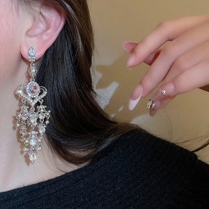 Detailed close-up of a long tassel heart earring with sparkling rhinestones on model's ear
