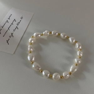 Macro shot of baroque freshwater pearls and gold beads on a textured cream leather background