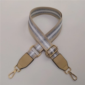Detail of adjustable beige woven bag strap with silver stripes and gold metal hooks