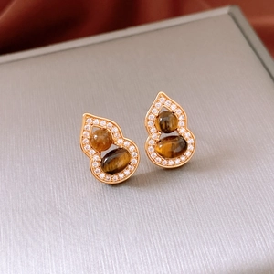 Détail macro de boucles d'oreilles gourde dorées avec œil de tigre et zircons