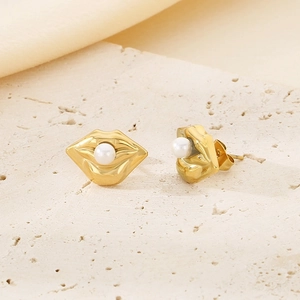 Detail of elegant gold lip-shaped earrings with a white pearl on a textured stone surface