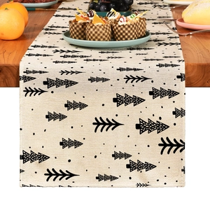 Beige linen Christmas table runner with black tree prints on a rustic wooden dining table