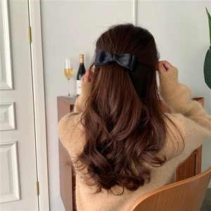 Detail view of a black satin double-layered bow hair clip worn on long wavy hair back