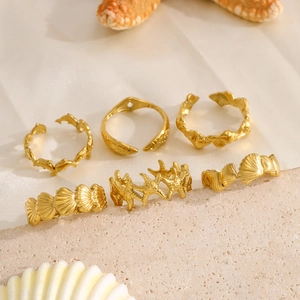 Summer ocean-themed gold ring set with starfish and seashell charms on sand background