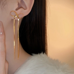 Vue détaillée de longues boucles d'oreilles nœud doré avec pompons portées par un modèle