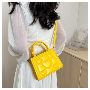 Sac à main jaune en cuir PU avec motif de cœurs, porté en bandoulière sur robe blanche